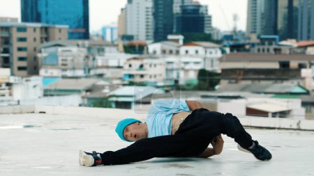 Téléchargez les photos : Danseur B-boy caucasien qualifié pratiquant la danse de rue sur le toit avec des sites urbains ou urbains. Prise de vue en mouvement d'un jeune homme exécutant une danse de rue en posant sur gel. Sport de plein air 2024. Endeavor. - en image libre de droit