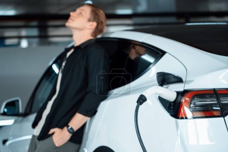 Photo for Young man travel with EV electric car to shopping center parking lot charging in downtown city showing urban sustainability lifestyle by green clean rechargeable energy of electric vehicle innards - Royalty Free Image