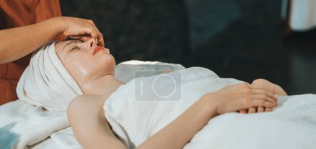 Téléchargez les photos : Une belle jeune femme caucasienne se fait masser le visage tout en étant allongée sur un lit de spa entouré d'un équipement de beauté électrique. Masque facial beauté. Entouré d'équipement médical au salon de spa. Tranquillité. - en image libre de droit