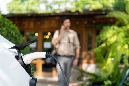 Photo for Focused EV electric car recharging at outdoor coffee cafe in springtime garden with blur background of eco friendly man, green city sustainability and environmental friendly EV vehicle. Expedient - Royalty Free Image