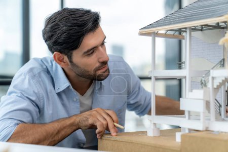 Photo for Closeup portrait of smart caucasian architect engineer inspect house model while thinking about building construction at architect studio on table with project plan, blueprint, equipment. Tracery. - Royalty Free Image
