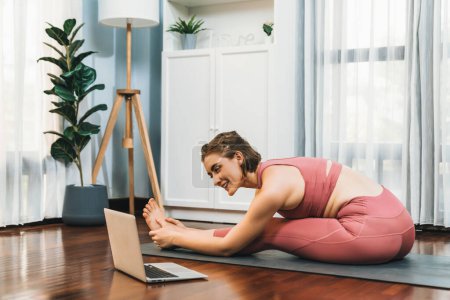 Photo for Flexible and dexterity woman in sportswear doing yoga position in meditation posture on exercising mat at home. Healthy gaiety home yoga online training session with peaceful mind and serenity. - Royalty Free Image