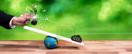 Photo for Businessman balance tree sprout on scale with CO2 emission icon, demonstrate ESG or environment social governance commitment to carbon reduction through clean energy technology. Panorama Reliance - Royalty Free Image