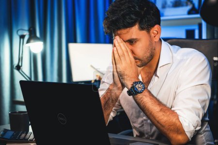 Photo for Stressful working businessman waiting email sending back for deadline project at night time, solving issue problem with under high pressure feeling on laptop with at neon light of workplace. Sellable. - Royalty Free Image