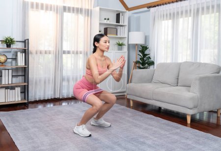 Foto de Mujer vigorosa y enérgica haciendo ejercicio en casa. Joven atlético asiático mujer fuerza y resistencia entrenamiento sesión como casa entrenamiento rutina con sentadilla. - Imagen libre de derechos