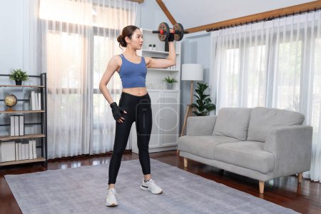 Photo for Vigorous energetic woman doing dumbbell weight lifting exercise at home. Young athletic asian woman strength and endurance training session as home workout routine. - Royalty Free Image