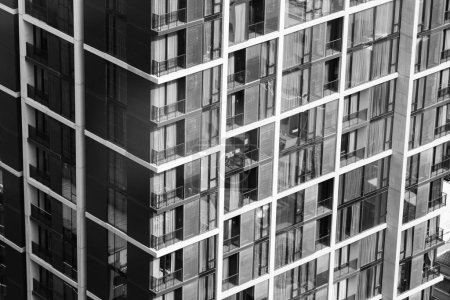 Foto de Ventana residencial edificio apartamento. Rascacielos de la ciudad moderna a la luz del día. Ventanas de apartamentos en modernos skylines con luz de día con filtro monocromo. Bienes raíces. Primer plano. Vista lateral. Adornado. - Imagen libre de derechos