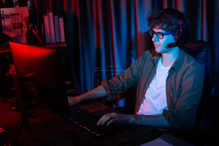 Photo for Smiling young gaming streamer team playing with joystick on Esport online on pc fighting game, try to win competitors on strategy planning for next harder at red neon lighting modern room. Gusher. - Royalty Free Image
