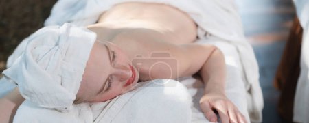 Téléchargez les photos : Un portrait d'une belle jeune femme caucasienne avec serviette blanche repose sur un lit de spa confortable avec détente. Gros plan de belle peau prête pour un massage du corps. Tranquillité. - en image libre de droit