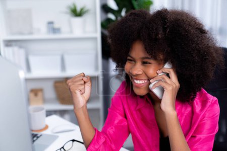 Téléchargez les photos : Femme africaine parlant avec un collègue ou un ami au téléphone et regardant l'écran avec un visage heureux. Réalisation pour la promotion du poste de travail dans l'entreprise avec la bonne nouvelle de la vie. Tastemaker. - en image libre de droit