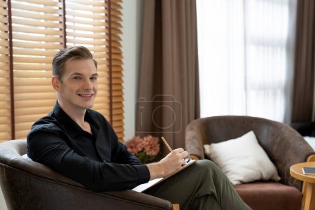 Téléchargez les photos : Portrait de psychologue homme heureux et souriant portrait assis sur un fauteuil dans un bureau de psychiatre ou une salle de thérapie. Conseiller et thérapeute en santé mentale amical et professionnel. Dévoilement - en image libre de droit