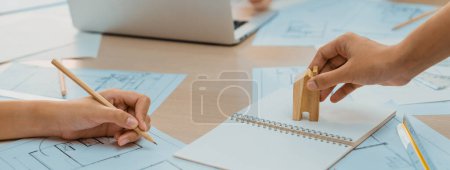 Photo for Professional architect hand draws a blueprint on table with architectural document and wooden block scatter around at office. Design and Planing concept. Focus on hand. Closeup. Delineation. - Royalty Free Image