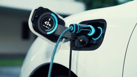 Photo for EV charger from home charging station plugged in and recharging electric car displaying digital battery status hologram. Smart and futuristic home energy infrastructure. Peruse - Royalty Free Image