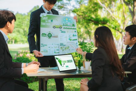 Téléchargez les photos : Groupe de gens d'affaires asiatiques présentant un plan de développement respectueux de l'environnement et un projet de technologie durable pour un avenir plus vert, établissant un bureau d'affaires écologique en plein air au parc naturel. - en image libre de droit