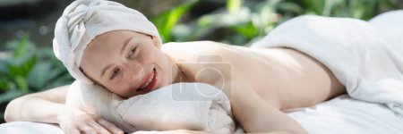Foto de Hermosa joven mujer se relaja en una cama de spa rodeada de naturaleza. listo para un masaje corporal. Atractiva hembra en toalla blanca tumbada en paz durante la espera de masaje corporal. De cerca. Tranquilidad - Imagen libre de derechos