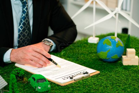 Téléchargez les photos : Homme d'affaires ou PDG en fonction signant un accord de réglementation environnementale pour sauver la Terre grâce à l'utilisation durable de l'énergie et à la réduction des émissions de CO2 pour un avenir plus vert. Charmante. - en image libre de droit