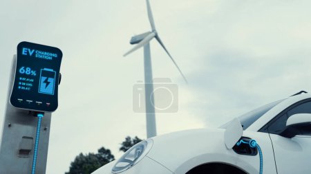 Photo for Electric car recharging energy from charging station by smart EV charger in wind turbine farm with nature outdoor background. Technological advance of alternative clean sustainable energy. Peruse - Royalty Free Image