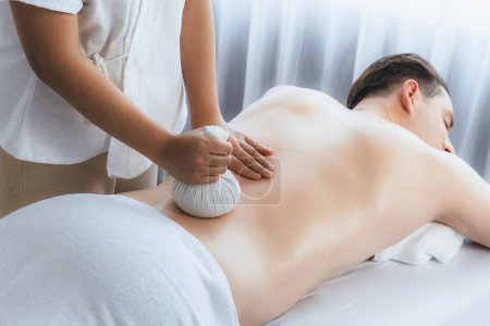 Photo for Hot herbal ball spa massage body treatment, masseur gently compresses herb bag on man body. Tranquil and serenity of aromatherapy recreation in day lighting ambient at spa salon. Quiescent - Royalty Free Image