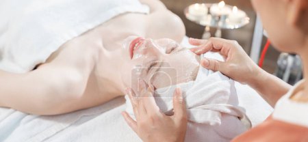 Téléchargez les photos : Portrait d'une belle femme caucasienne ayant un massage facial avec masque facial fait maison alors qu'elle se trouve sur un lit de spa entouré d'équipements électriques de beauté et d'un environnement naturel paisible. Tranquillité. - en image libre de droit