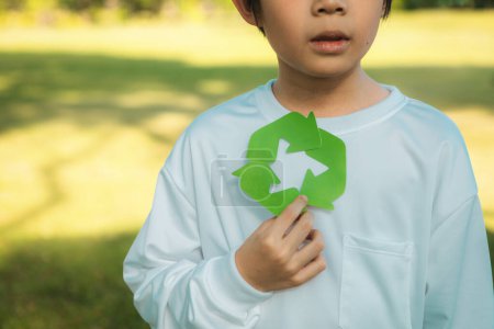 Téléchargez les photos : Joyeux jeune garçon asiatique tenant le symbole de recyclage sur le parc vert naturel de la lumière du jour promouvoir le recyclage des déchets, réduire et réutiliser les encouragements pour une sensibilisation éco durable pour les générations futures. Pneumatique - en image libre de droit
