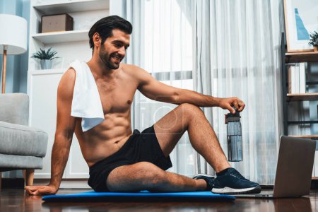 Photo for Athletic and sporty man resting on fitness mat during online body workout exercise session for fit physique and healthy sport lifestyle at home. Gaiety home exercise workout training concept. - Royalty Free Image
