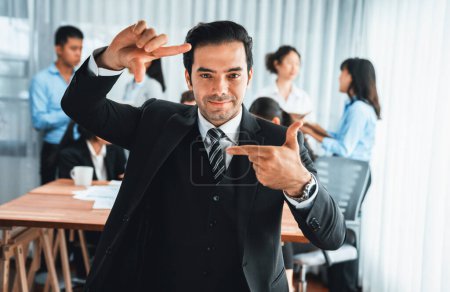 Photo for Portrait of happy businessman looking at camera, making hand holding gesture for advertising product with motion blur background of business people movement in dynamic business meeting. Habiliment - Royalty Free Image