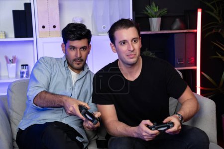 Photo for Winner and loser players of buddy friend gamers playing video game on TV using joysticks in studio room with neon blue light. Comfy living indoor at home place with cheerful fighting winner. Sellable. - Royalty Free Image