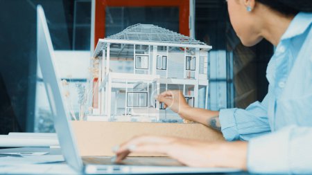 Photo for Closeup of hispanic architect hands engineer using laptop analysis house model structure. Project manager checking house model construction while typing on laptop. Design concept. Manipulator. - Royalty Free Image