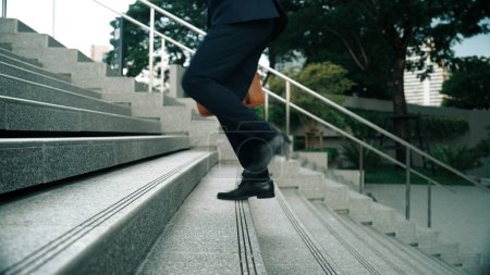 Photo for Skilled business man walking up stairs at park or city while holding bag in the hand Professional project manager going to workplace. Represent growth, getting promotion, increasing skill. Exultant. - Royalty Free Image