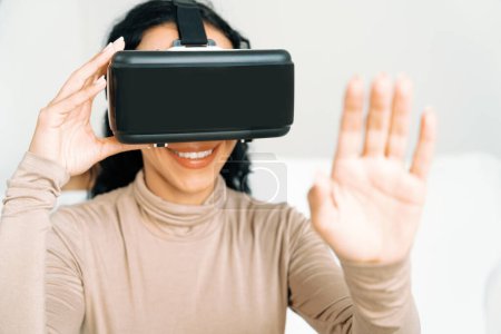 Photo for Young woman using virtual reality VR goggle at home for crucial online shopping experience. The virtual reality VR innovation optimized for female digital entertainment lifestyle. - Royalty Free Image