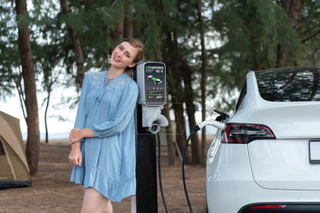 Photo for Holiday road trip vacation traveling to the beach camp with electric car, young woman recharge EV vehicle with green and clean energy. Beach travel camping with eco-friendly EV car .Perpetual - Royalty Free Image