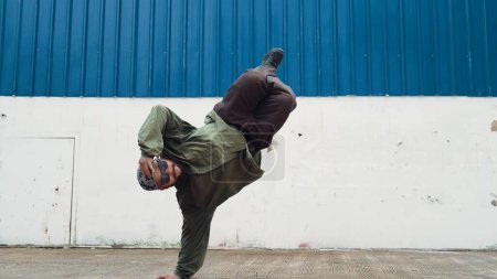 Photo for Hipster dancing b-boy foot step at street with blue wall. Asian break dancer practice street dance while stretch arms. Hip hop choreographer perform energetic dance. Outdoor sport 2024. Endeavor. - Royalty Free Image