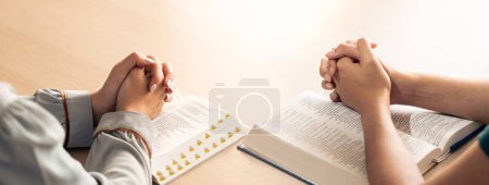 Photo for Two believer praying together on holy bible book faithfully with wooden cross placed at wooden church. Concept of hope, religion, faith, christianity and god blessing. Facing hand. Burgeoning. - Royalty Free Image