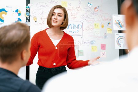 La líder femenina atractiva profesional presenta un plan de marketing creativo mediante el uso de un gráfico estadístico de mapas mentales de lluvia de ideas y una nota adhesiva colorida en la sala de reuniones de negocios moderna. Inmaculada.