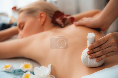 Photo for Closeup hot herbal ball spa massage body treatment, masseur gently compresses herb bag on woman body. Tranquil and serenity of aromatherapy recreation in day lighting ambient at spa salon. Quiescent - Royalty Free Image