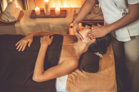 Photo for Caucasian woman enjoying relaxing anti-stress head massage and pampering facial beauty skin recreation leisure in warm candle lighting ambient salon spa in luxury resort or hotel. Quiescent - Royalty Free Image