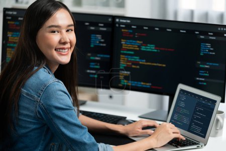 Photo for Young Asian in IT developer looking at camera to present with online information on pc with coding program data application, wearing jeans shirt. surround by safety analysis two screens. Stratagem. - Royalty Free Image