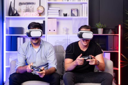 Photo for Buddy friend gamers playing video game using joysticks and VR headset of virtual technology in reality in studio room with neon blue light. Comfy living indoor with cheerful fighting winner. Sellable. - Royalty Free Image