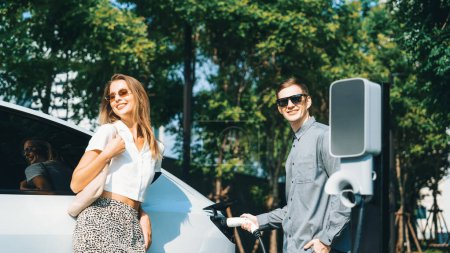 Téléchargez les photos : Les jeunes couples voyagent avec la recharge de voiture électrique EV dans le jardin extérieur vert de la ville durable en été montre mode de vie durable urbain par vert propre énergie rechargeable des entrailles de véhicule électrique - en image libre de droit