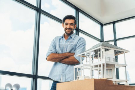 Photo for Portrait of architect engineer in casual outfit smile at camera while crossing arms. Businessman looking at camera and standing with arms folded near house model, architectural model. Tracery. - Royalty Free Image