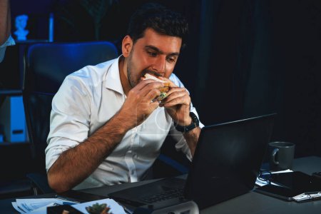 Photo for Coworker partners with happy smiling face eating delicious sandwich with coffee while working on laptop at night time. Hungry creative colleagues discussing new project website at workplace. Sellable. - Royalty Free Image