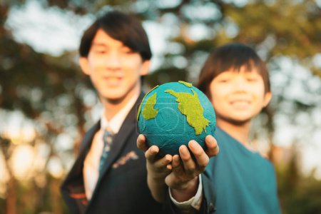 Téléchargez les photos : Focus La Terre avec un garçon asiatique flou et un homme d'affaires tenant le globe ensemble comme concept de journée de la Terre en tant que responsable social d'entreprise pour rendre l'environnement plus vert pour les générations futures durables. Pneumatique - en image libre de droit