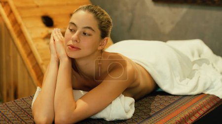 Foto de Retrato de una hermosa mujer caucásica en toalla blanca mujer se encuentra en la cama de spa frente a un gabinete de sauna de madera caliente con relajación y tranquilidad en el salón de spa. De cerca. Una vista lateral. Tranquilidad. - Imagen libre de derechos