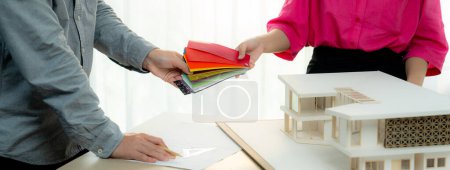 Photo for Female architect interior designer send color swatches to project manager for choosing an appropriate color with house model and architectural equipment placed on meeting table. Variegated. - Royalty Free Image