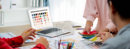 Photo for A portrait of creativity graphic designer team select appropriate color for the project by using laptop on table with equipment and designing tool scatter around at modern office. Closeup. Variegated. - Royalty Free Image
