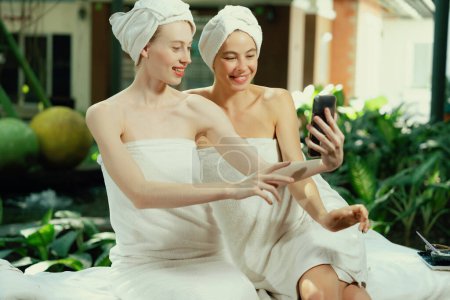 Photo for Couple of young beautiful women with beautiful skin in white towel taking a photo together at outdoor surrounded by peaceful natural environment. Beauty and healthy spa concept. Tranquility. - Royalty Free Image