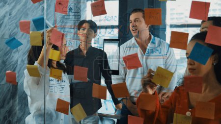 Photo for Portrait of professional business team brainstorming marketing idea by using sticky notes to share creative idea at glass wall. Group of diverse business team discuss about strategy. Manipulator. - Royalty Free Image