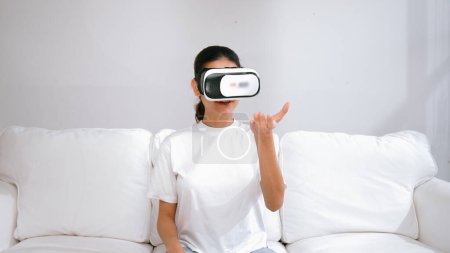 Téléchargez les photos : Jeune femme utilisant réalité virtuelle VR masque à la maison pour vivre l'expérience d'achat en ligne. L'innovation VR en réalité virtuelle optimisée pour le divertissement numérique féminin. - en image libre de droit