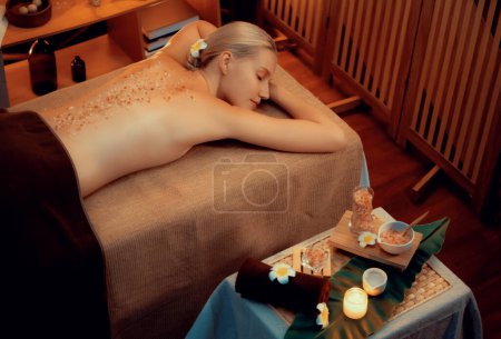 Téléchargez les photos : Femme client ayant un traitement d'exfoliation dans un salon de spa de luxe avec lumière de bougie de chaleur ambiante. Soin de beauté au gommage au sel dans le gommage corporel du spa de santé. Tranquillité - en image libre de droit