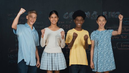Photo for Diverse academic student cheering and celebrate successful project while raised hand. Group of multicultural children standing at blackboard with engineering code while looking at camera. Edification. - Royalty Free Image